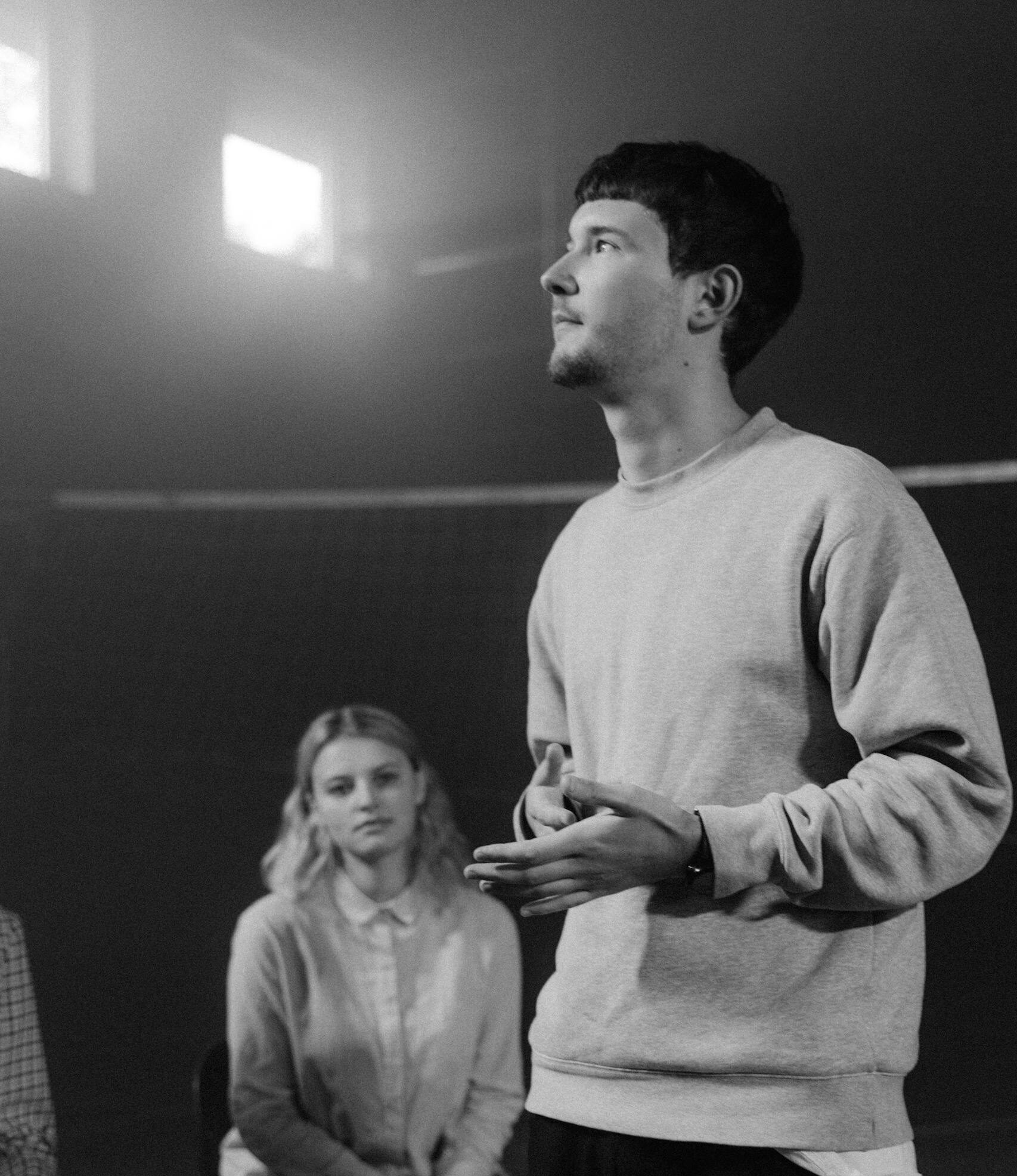 A young man speaks passionately during a group therapy session, in a monochrome setting.