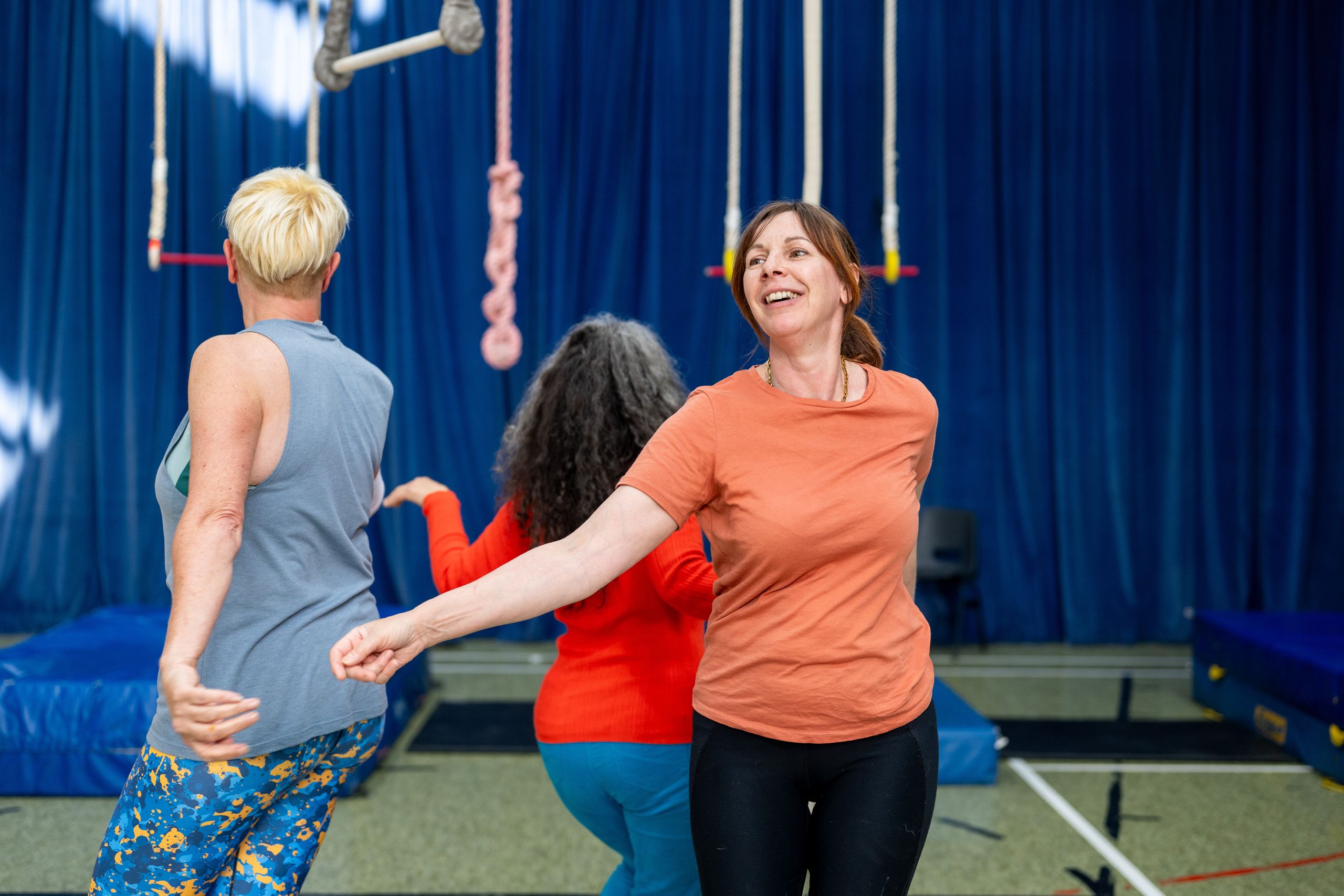 Group of adults engaging in a trapeze rehearsal indoors, smiling and having fun.