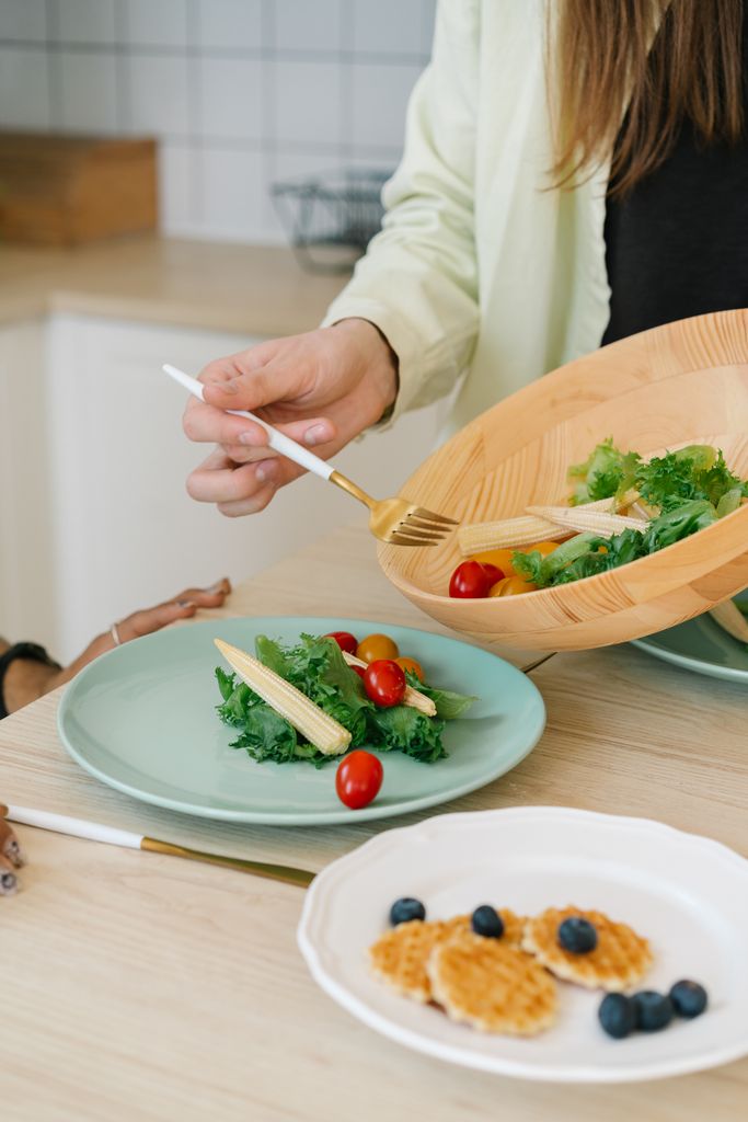 Person serving a fresh salad with baby corn, tomatoes, and greens for a healthy meal.
